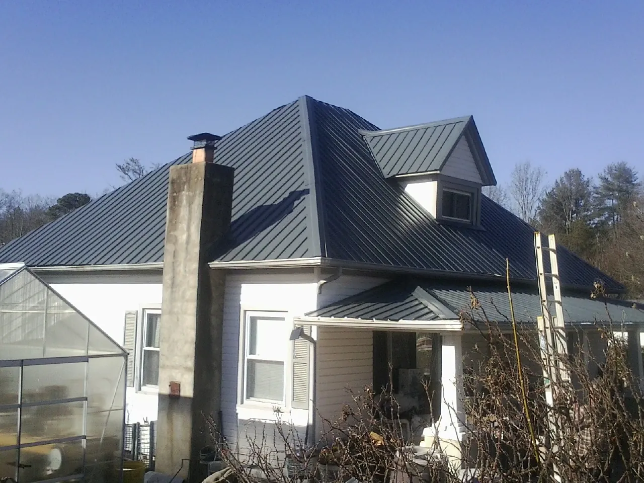 Dark blue standing seam metal roof on a white farmhouse with dormer — Slate & Tile Roof Repair by Roofing Brothers in Prompton