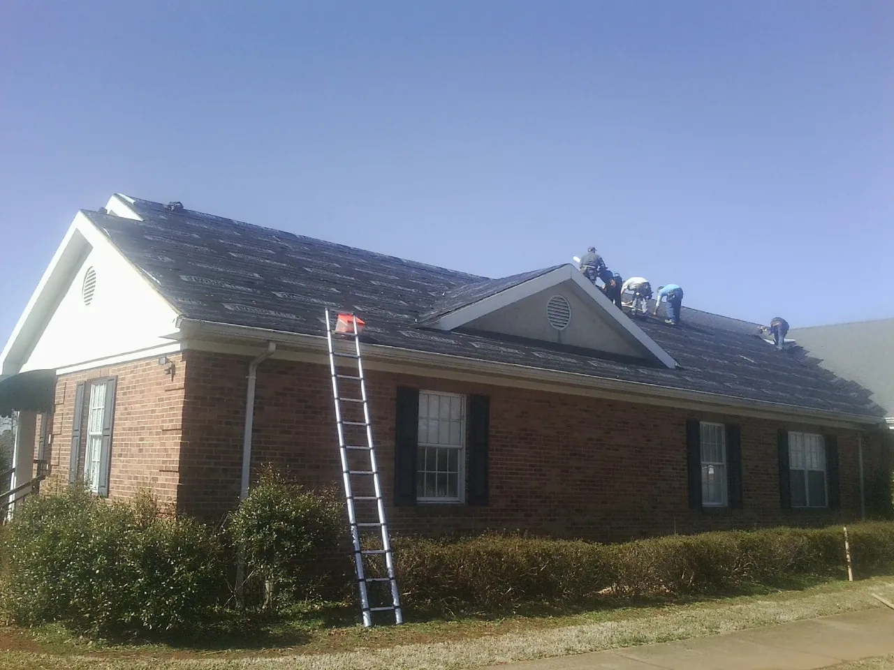 Crew tearing shingles off a brick ranch roof with a ladder set — Emergency Roof Repair work by our crew in Prompton