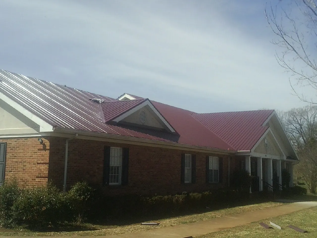 Red metal roof with gabled entries on a long brick building, from a Hail Damage Roof Repair job in Prompton