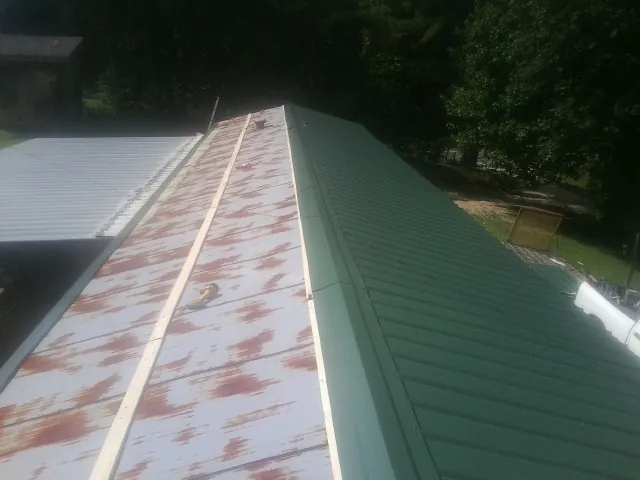 Old rusted panels beside newly installed green metal roofing — Wind Damage Roof Repair by Roofing Brothers in Prompton