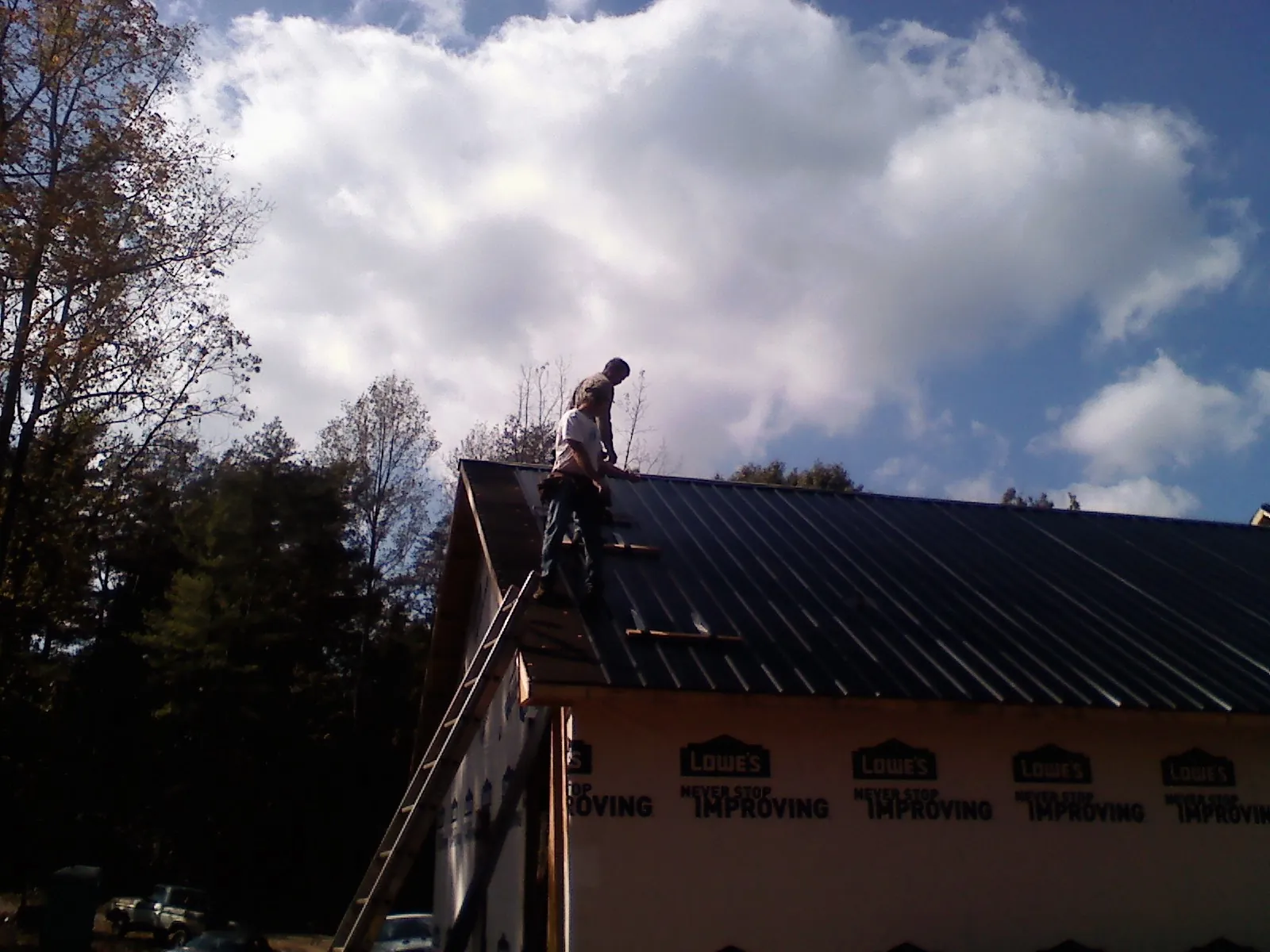 Roofer fastening dark metal panels high against a cloudy sky, from a Roof Inspection job in Prompton